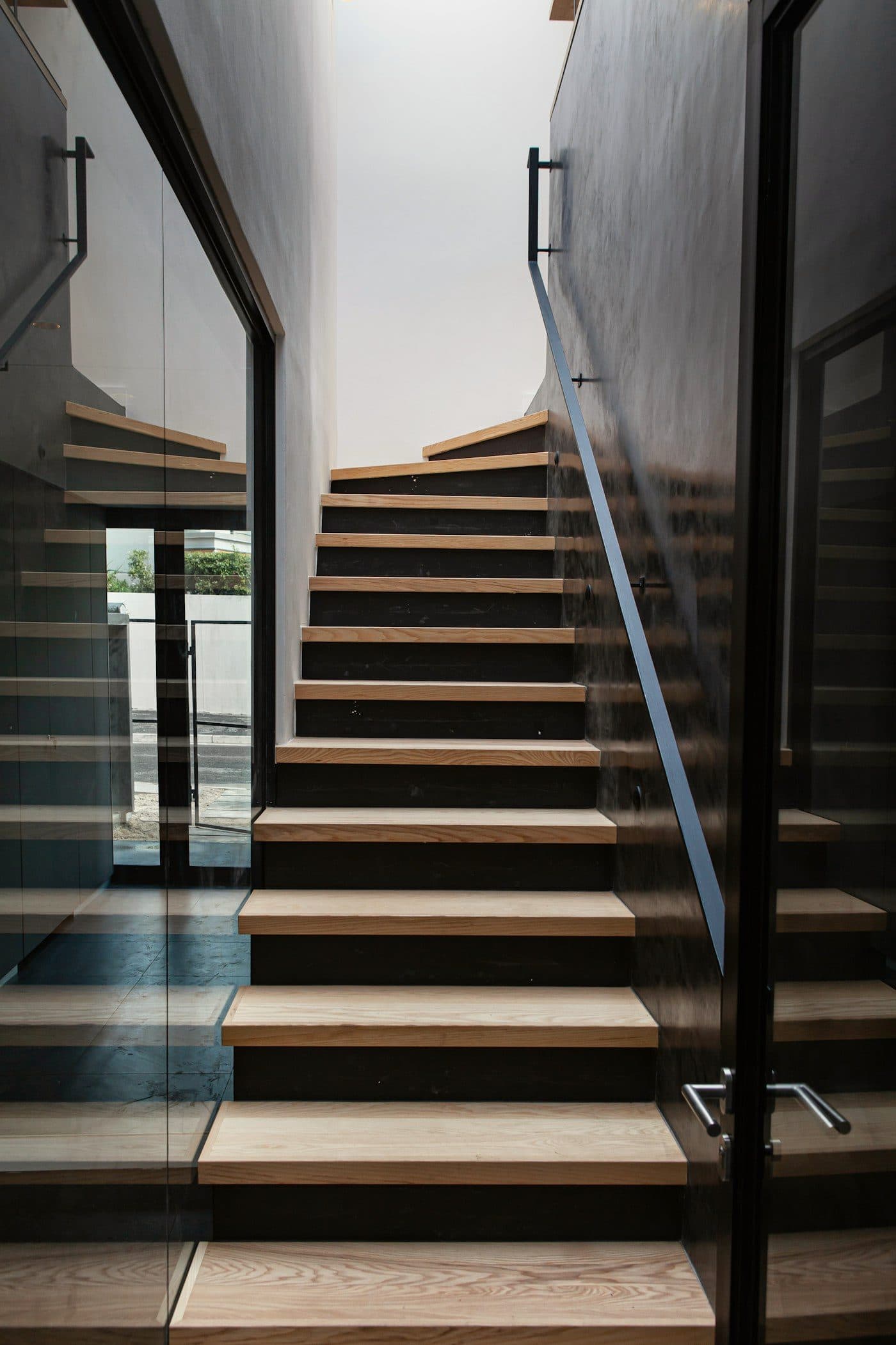 Oak stair treads on a dark steel stringer, with a slim steel handrail and frameless glass alongside.