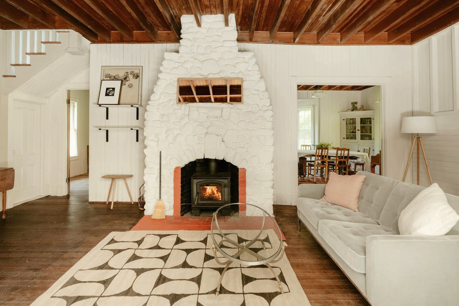 Renovated living room in an older house: painted stone fireplace, exposed ceiling joists and wide plank floors.